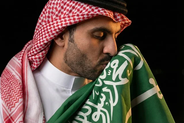 Gestures of pride and joy in belonging to the homeland, commemorating Saudi National Day on September 23, Saudi Flag Day on March 11, an Arab Saudi man wearing the ghutrah and traditional thobe kissing the flag of the Kingdom, the day we began in 1727 AD.