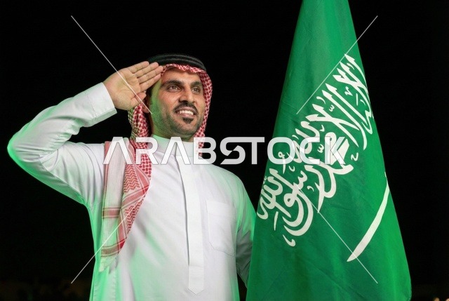 إيماءات الفخر و السرور بالانتماء للوطن, إحياء ذكرى اليوم الوطني السعودي 23 سبتمبر، يوم العلم السعودي 11 مارس, رجل عربي سعودي يرتدي الشماغ والثوب التقليدي يلقي التحية امام علم المملكة، يوم بدينا 1727 م