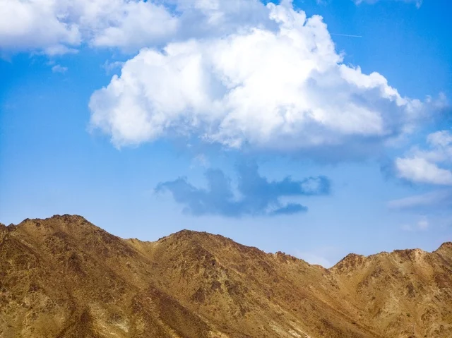 منظر السماء المبلدة بالغيوم فوق جبال مدينة حتا السياحية بإمارة دبي بدولة الإمارات العربية المتحدة ، المرتفعات الجبلية ، خلفية الطبيعة الجبلية ، السياحة في الإمارات ، جبال حتا