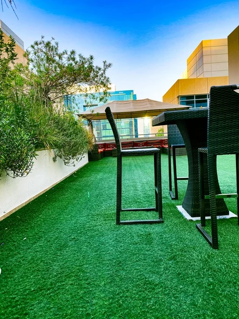 حديقة خارجية عصرية في دبي، مساحات خضراء مزينة بالزهور والنباتات، جلسات استرخاء في فناء مبنى حديث، أجواء هادئة تجمع بين الطبيعة والتصميم المعماري الحديث، نمط حياة راقي في دولة الإمارات العربية المتحدة.