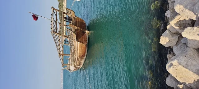 The towers and skyscrapers on the waterfront in the city of Qatar are tourist spots for enjoying pleasant times, a wooden boat in the middle of the sea, enjoying calm marine trips and picnics, the architectural engineering art of the buildings and facilities overlooking the Doha Corniche.