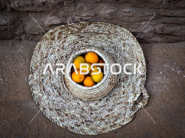 مجموعة من حبات البرتقال الطازج في سلة تقليدية مصنوعة من القش، المزارع والواحات الخصبة في البلدة القديمة بالعلا، منتجات وطنية محلية، المناظر الطبيعية المتميزة في المملكة العربية السعودية، محمية طبيعية لزراعة الاشجار