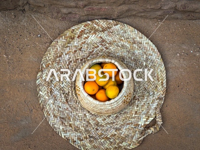 مجموعة من حبات البرتقال الطازج في سلة تقليدية مصنوعة من القش، المزارع والواحات الخصبة في البلدة القديمة بالعلا، منتجات وطنية محلية، المناظر الطبيعية المتميزة في المملكة العربية السعودية، محمية طبيعية لزراعة الاشجار