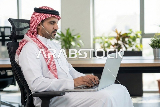 Completing the required tasks, Saudi office professions and jobs, managing and organizing company affairs through technical devices, integrating work with technology, an Arab Gulf Saudi businessman wearing traditional attire and a ghutrah working on a laptop, working in the economic field.