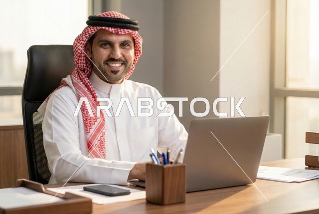 إنجاز المهام المطلوبة، مهن ووظائف مكتبية سعودية، إدارة شؤون الشركة وتنظيمها عبر الاجهزة التقنية، دمج العمل مع التكنولوجيا، رجل أعمال عربي خليجي سعودي يرتدي الزي التقليدي والشماغ يعمل على الحاسوب المحمول, العمل في المجال الاقتصادي