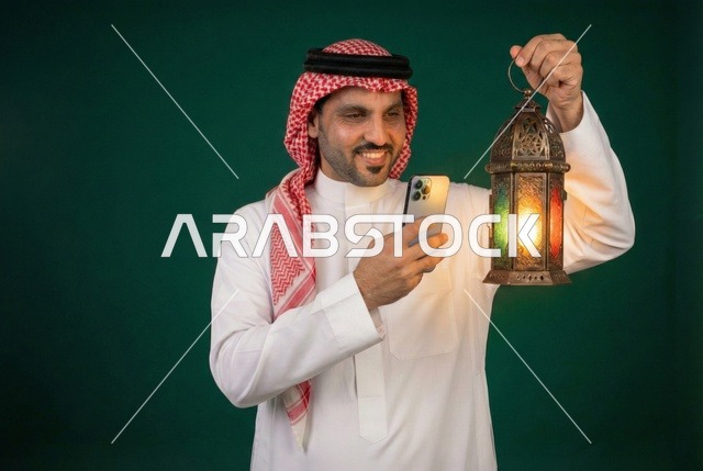 التقاط الصور التذكارية عبر الجوال ، شهر رمضان المبارك، رجل عربي خليجي سعودي يرتدي الزي التقليدي والشماغ  يمسك فانوس رمضان، إضاءة وزينة شهر رمضان، أجواء رمضانية، مناسبات دينية ، اسلاميات وعبادات