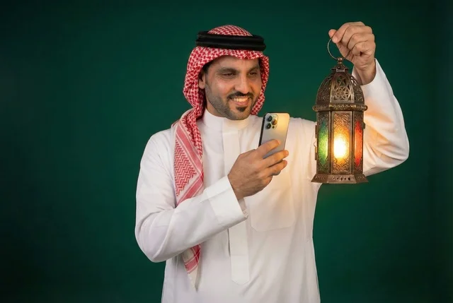 التقاط الصور التذكارية عبر الجوال ، شهر رمضان المبارك، رجل عربي خليجي سعودي يرتدي الزي التقليدي والشماغ  يمسك فانوس رمضان، إضاءة وزينة شهر رمضان، أجواء رمضانية، مناسبات دينية ، اسلاميات وعبادات