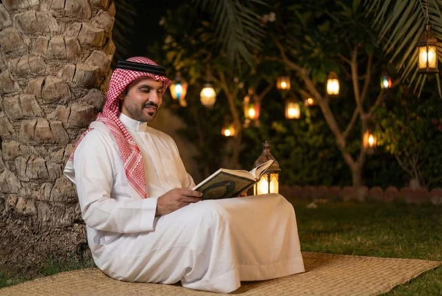 رجل عربي خليجي سعودي  يرتدي الزي التقليدي والشماغ يقرأ القرآن الكريم، المصحف الشريف، تلاوة وحفظ القران الكريم، فانوس رمضان، استقبال شهر رمضان المبارك، زينة شهر رمضان، أجواء رمضانية، جلسة خارجية في الهواء الطلق