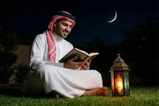 A Saudi Arabian Gulf man wearing traditional attire and a shemagh reads the Holy Quran, the noble Quran, reciting and memorizing the Quran, a Ramadan lantern, welcoming the blessed month of Ramadan, Ramadan decorations, Ramadan atmosphere, an outdoor gathering in the open air.