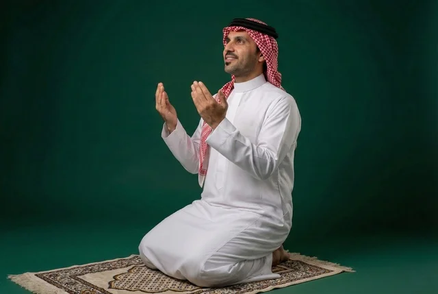 Remembrances, supplications, and obligations, bowing, prostration, and humility before God. An Arab Saudi Gulf man wearing traditional attire and a headscarf sits on the prayer rug and performs the obligatory prayer, performing the Taraweeh prayer during the holy month of Ramadan, supplicating and beseeching God.
