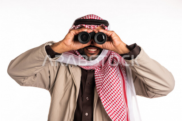 بورتريه لرجل عربي خليجي سعودي يرتدي ملابس الشتاء الدافئة، النظر من خلال الناظور، إيماءات وجه تدل على الدهشة والتعجب، ملابس لتدفئة الجسم، الاستكشاف والمغامرة، فريق الكشافة، رؤية مستقبلية، التخطيط المستقبلي، اهداف وطموحات، اجواء شتوية، خلفية بيضاء