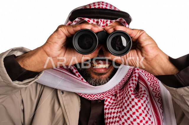 بورتريه لرجل عربي خليجي سعودي يرتدي ملابس الشتاء الدافئة، النظر من خلال الناظور، إيماءات وجه تدل على الدهشة والتعجب، ملابس لتدفئة الجسم، الاستكشاف والمغامرة، فريق الكشافة، رؤية مستقبلية، التخطيط المستقبلي، اهداف وطموحات، اجواء شتوية، خلفية بيضاء