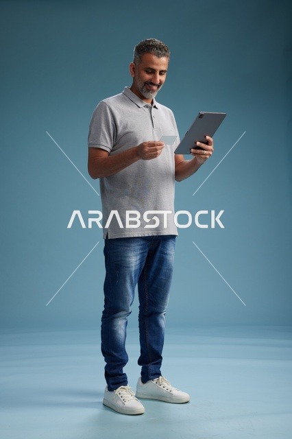 رجل عربي سعودي خليجي يرتدي الزي الكاجوال يمسك بيده جهاز لوحي, ايماءات وحركات متنوعه, الجسم بالطول, الكامل خلفيه زرقاء