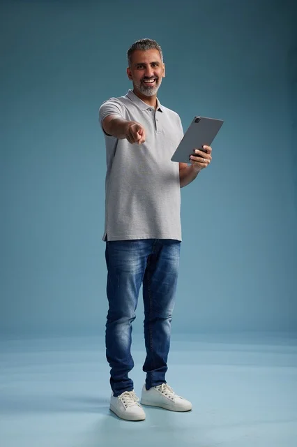 A Saudi Arabian Gulf man wearing casual attire is holding a tablet in his hand, with various gestures and movements, full-body, against a blue background.