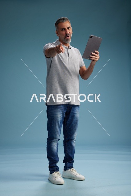 رجل عربي سعودي خليجي يرتدي الزي الكاجوال يمسك بيده جهاز لوحي, ايماءات وحركات متنوعه, الجسم بالطول, الكامل خلفيه زرقاء
