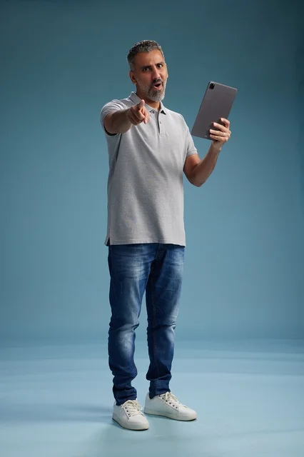 رجل عربي سعودي خليجي يرتدي الزي الكاجوال يمسك بيده جهاز لوحي, ايماءات وحركات متنوعه, الجسم بالطول, الكامل خلفيه زرقاء