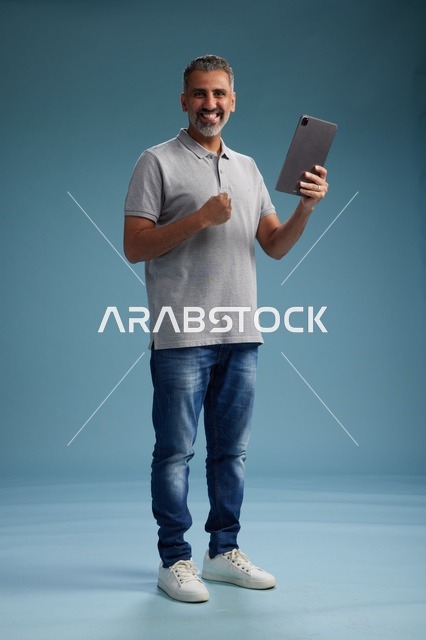 رجل عربي سعودي خليجي يرتدي الزي الكاجوال يمسك بيده جهاز لوحي, ايماءات وحركات متنوعه, الجسم بالطول, الكامل خلفيه زرقاء