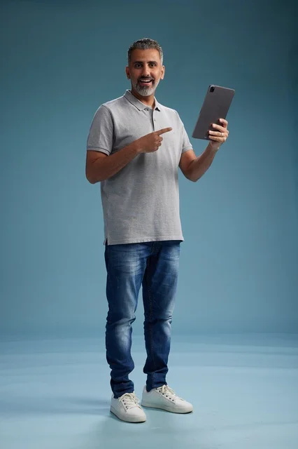 A Saudi Arabian Gulf man wearing casual attire is holding a tablet in his hand, with various gestures and movements, full-body, against a blue background.
