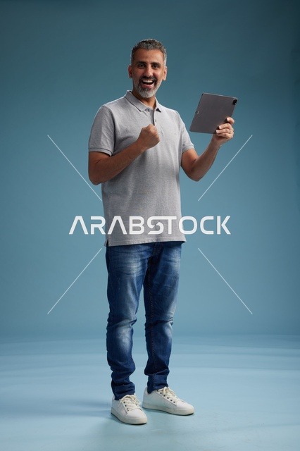 رجل عربي سعودي خليجي يرتدي الزي الكاجوال يمسك بيده جهاز لوحي, ايماءات وحركات متنوعه, الجسم بالطول, الكامل خلفيه زرقاء