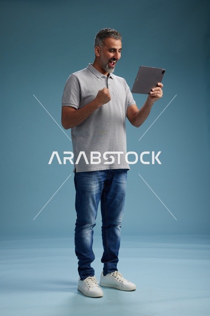 رجل عربي سعودي خليجي يرتدي الزي الكاجوال يمسك بيده جهاز لوحي, ايماءات وحركات متنوعه, الجسم بالطول, الكامل خلفيه زرقاء