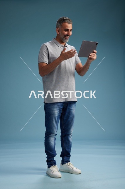 رجل عربي سعودي خليجي يرتدي الزي الكاجوال يمسك بيده جهاز لوحي, ايماءات وحركات متنوعه, الجسم بالطول, الكامل خلفيه زرقاء