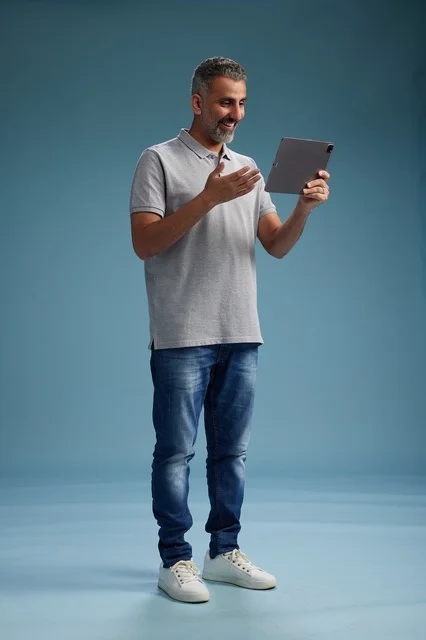 A Saudi Arabian Gulf man wearing casual attire is holding a tablet in his hand, with various gestures and movements, full-body, against a blue background.