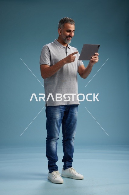 رجل عربي سعودي خليجي يرتدي الزي الكاجوال يمسك بيده جهاز لوحي, ايماءات وحركات متنوعه, الجسم بالطول, الكامل خلفيه زرقاء