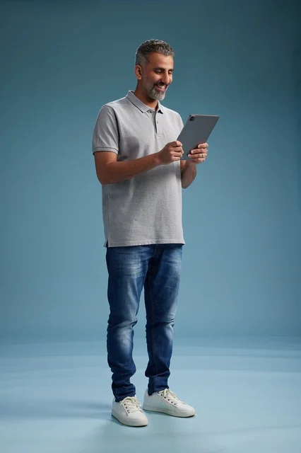 A Saudi Arabian Gulf man wearing casual attire is holding a tablet in his hand, with various gestures and movements, full-body, against a blue background.