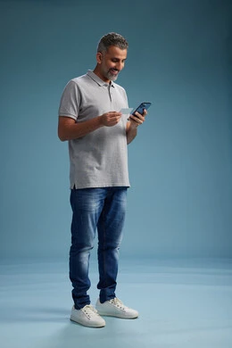 رجل عربي سعودي خليجي يرتدي الزي الكاجوال يقوم باجراء مكالمه هاتفيه ويحمل بطاقه بيضاء فارغه, كرت تعريفي , الجسم بالطول اكامل, خلفيه زرقاء