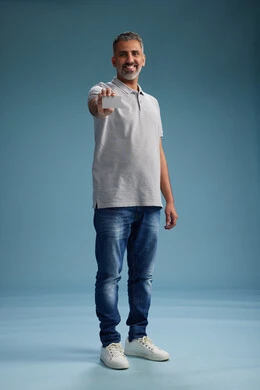 A Saudi Arabian Gulf Arab man wearing casual attire holding a blank white card, full body, blue background.