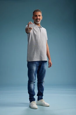 A Saudi Arabian Gulf Arab man wearing casual attire holding a blank white card, full body, blue background.
