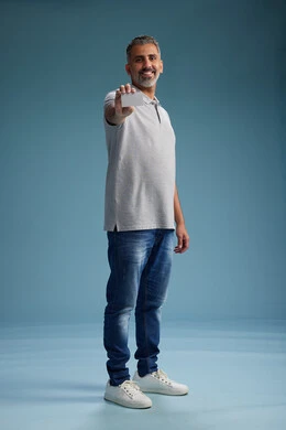 A Saudi Arabian Gulf Arab man wearing casual attire holding a blank white card, full body, blue background.