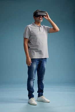 A Saudi Arabian Gulf Arab man wearing casual attire is using virtual reality glasses, watching movies and entertaining videos through VR, full body, with a blue background.