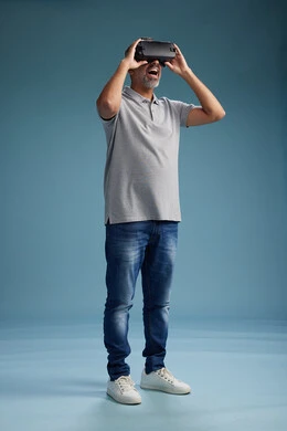 A Saudi Arabian Gulf Arab man wearing casual attire is using virtual reality glasses, watching movies and entertaining videos through VR, full body, with a blue background.