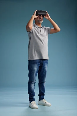 A Saudi Arabian Gulf Arab man wearing casual attire is using virtual reality glasses, watching movies and entertaining videos through VR, full body, with a blue background.