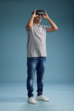 رجل عربي سعودي خليجي يرتدي الزي الكاجوال يستخدم نظارة الواقع الافتراضي, مشاهدة الافلام والفيديوز المسليه عبر الفي ار, كامل الجسم, خلفيه زرقاء