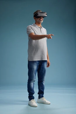 A Saudi Arabian Gulf Arab man wearing casual attire is using virtual reality glasses, watching movies and entertaining videos through VR, full body, with a blue background.