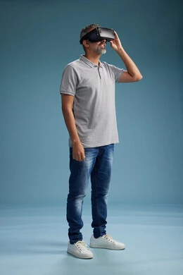 A Saudi Arabian Gulf Arab man wearing casual attire is using virtual reality glasses, watching movies and entertaining videos through VR, full body, with a blue background.