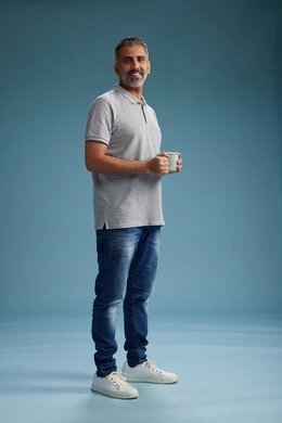 A Saudi Arabian Gulf Arab man enjoying a cup of coffee in casual clothes, full body, blue background.