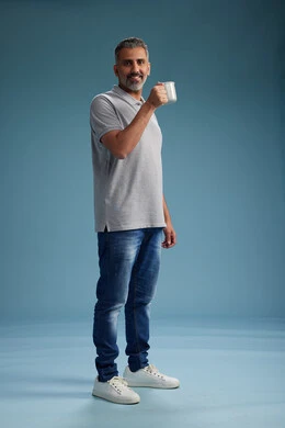 A Saudi Arabian Gulf Arab man enjoying a cup of coffee in casual clothes, full body, blue background.