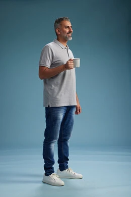 A Saudi Arabian Gulf Arab man enjoying a cup of coffee in casual clothes, full body, blue background.
