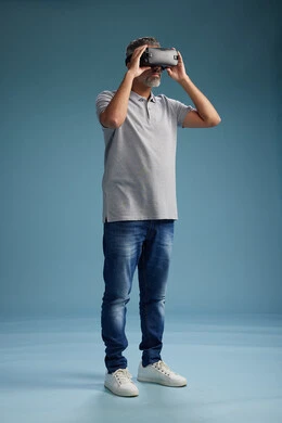 A Saudi Arabian Gulf Arab man wearing casual attire is using virtual reality glasses, watching movies and entertaining videos through VR, full body, with a blue background.