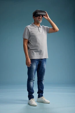 A Saudi Arabian Gulf Arab man wearing casual attire is using virtual reality glasses, watching movies and entertaining videos through VR, full body, with a blue background.