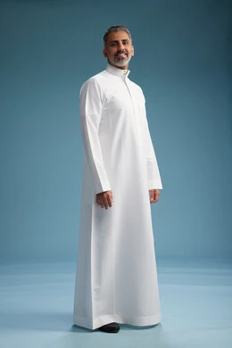 رجل عربي  سعودي خليجي يرتدي ثوب ابيض  , النظر الى شيء ما, الوقوف بثقه, كامل الجسم, خلفيه زرقاء