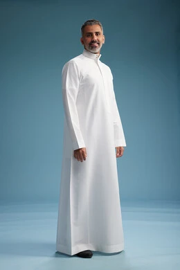 رجل عربي  سعودي خليجي يرتدي ثوب ابيض  , النظر الى شيء ما, الوقوف بثقه, كامل الجسم, خلفيه زرقاء