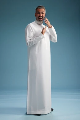 A Saudi Arabian man from the Gulf region, wearing a white thobe, makes a phone call with various gestures and movements, communicating with friends via mobile phone, full body, blue background. A Saudi Arabian man from the Gulf region, wearing a white thobe, makes a phone call with various gestures and movements, communicating with friends via mobile phone, full body, blue background.