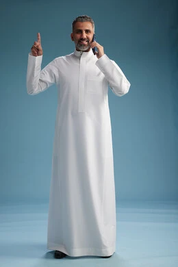 رجل  عربي سعودي خليجي يرتدي الثوب الابيض يجري مكالمة هاتفية بايماءات وحركات متنوعه, التواصل مع الاصدقاء عبر الجوال, كامل الجسم, خلفيه زرقاء