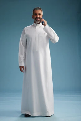 رجل  عربي سعودي خليجي يرتدي الثوب الابيض يجري مكالمة هاتفية بايماءات وحركات متنوعه, التواصل مع الاصدقاء عبر الجوال, كامل الجسم, خلفيه زرقاء