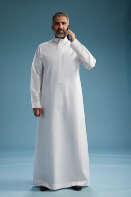 A Saudi Arabian man from the Gulf region, wearing a white thobe, makes a phone call with various gestures and movements, communicating with friends via mobile phone, full body, blue background.