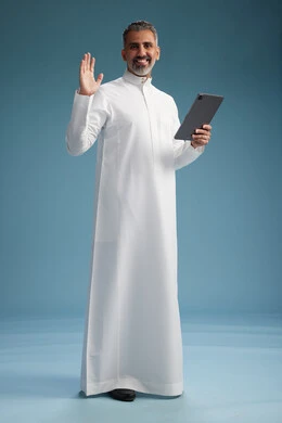 بورتريه لرجل عربي سعودي  خليجي يرتدي الثوب  الابيض يستخدم جهازاً لوحياً رقمياً, كامل الجسم, خلفيه زرقاء